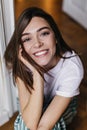 Cute dark-eyed girl smiling to camera while chilling at home. Indoor overhead photo of brunette att