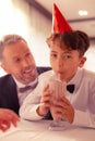 Cute dark-eyed grandson drinking milk cocktail near his granddad