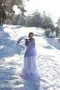 Vertical portrait of a cute European woman in a long white dress and a light purple openwork shawl against the winter landscape Royalty Free Stock Photo