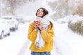 Cute dark-haired girl in a yellow sweater, jeans and a white scarf standing with a red mug on a snowy street on a winter Royalty Free Stock Photo