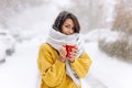 Cute dark-haired girl in a yellow sweater, jeans and a white scarf standing with a red mug on a snowy street on a winter Royalty Free Stock Photo