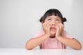 Cute dark haired little girl with a bored face sitting at a table on a white background