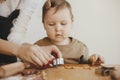 Cute daughter and mother making together christmas cookies on messy table. Adorable toddler girl helper with mom cutting dough for Royalty Free Stock Photo