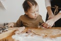 Cute daughter and mother making together christmas cookies on messy table. Adorable toddler girl helper with mom cutting dough for Royalty Free Stock Photo