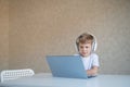 Cute diligent boy is typing on the keyboard and is carefully looking at the laptop screen. Caucasian schoolboy sits at a