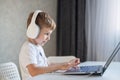 Cute diligent boy is typing on the keyboard and is carefully looking at the laptop screen. Caucasian schoolboy sits at a Royalty Free Stock Photo