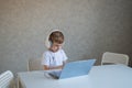 Cute diligent boy is typing on the keyboard and is carefully looking at the laptop screen. Caucasian schoolboy sits at a Royalty Free Stock Photo