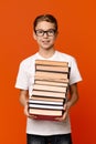 Cute diligent student boy in glasses with heap of books