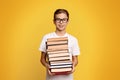 Cute diligent student boy in glasses with heap of books