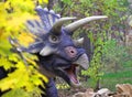 cute dinosaur Triceratops looks out from behind a bush in a green meadow