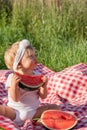 Cute dirty caucasian blonde baby girl eating fresh red watermelon at picnic in summer sunny weather. Healthy food for