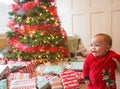 Cute diverse little boy smiling on Christmas morning in front of a Christmas tree