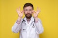 Cute doctor holds glasses in hands and looks through them, with a funny, benevolent expression on face. Yellow