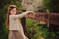 Cute dreamy kid girl in beige outfit climbing rustic wooden fence in spring garden Royalty Free Stock Photo