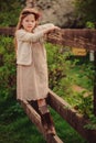 Cute dreamy kid girl in beige outfit climbing rustic wooden fence in spring garden Royalty Free Stock Photo