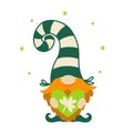 A cute dwarf holds a green heart with shamrock in his hands. Red-bearded elf for good luck. Irish gnome in a striped