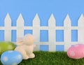 Cute Easter image with green grass, colorful sparkly eggs, a ceramic bunny and a white picket fence.