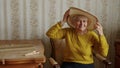 cute elder woman sitting on the chair and adjusting her summer hat medium shot living room seniority concept