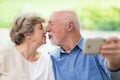 Elderly couple kissing in front of a mobile phone while taking selfie Royalty Free Stock Photo