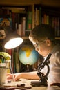 Cute elementary school boy looking into microscope at his desk at home. Young scientist making experiments in his home laboratory Royalty Free Stock Photo