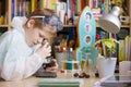 Cute elementary school boy looking into microscope at his desk at home. Young scientist making experiments in his home laboratory Royalty Free Stock Photo