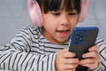 Cute elementary school girl wearing headphones holding a smartphone. Happy Asian girl studying online on smartphone or Royalty Free Stock Photo