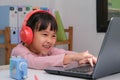 Cute elementary school girl wearing headphones and using a laptop computer. Happy Asian kids study online interactively with Royalty Free Stock Photo