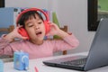 Cute elementary school girl wearing headphones and using a laptop computer. Happy Asian kids study online interactively with Royalty Free Stock Photo