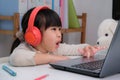 Cute elementary school girl wearing headphones and using a laptop computer. Happy Asian kids study online interactively with Royalty Free Stock Photo