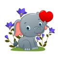 The cute elephant is sitting and holding the love balloon with his trunk in the garden Royalty Free Stock Photo