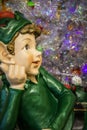 Cute elf figurine dressed in green relaxing in front of silver bokeh Christmas tree Closeup and selective focus