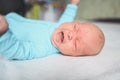 Cute emotional crying newborn infant boy in blue jumpsuit laying on bed. Baby facial expressions