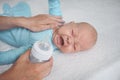 Cute emotional crying newborn infant boy laying on bed with milk bottle. Baby facial expressions