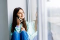 A cute emotional girl child talking on a mobile phone on the windowsill, chatting and talking with friends, addiction to gadgets, Royalty Free Stock Photo