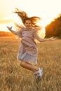 Cute emotional smiling girl with long hair cheerfully jumping in the field in sunset at a summer evening. Royalty Free Stock Photo