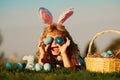 Cute excited bunny child boy with rabbit ears. Child with easter eggs in basket outdoor. Boy laying on grass in park