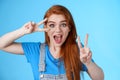 Cute excited redhead enthusiastic girl smiling, look joyful show peace, victory signs near face, optimistic lucky