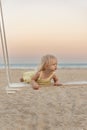 Cute fair-haired girl get on the swings on sandy beach. Little girl has fun by the sea during sunset Royalty Free Stock Photo