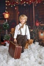 Cute fashion toddler boy, playing in the snow with teddy bear in front of a wooden cabin log Royalty Free Stock Photo