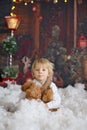 Cute fashion toddler boy, playing in the snow with teddy bear in front of a wooden cabin log Royalty Free Stock Photo