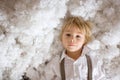 Cute fashion toddler boy, playing in the snow with teddy bear in front of a wooden cabin log