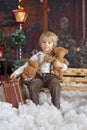 Cute fashion toddler boy, playing in the snow with teddy bear in front of a wooden cabin log Royalty Free Stock Photo