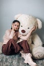 Cute fashionable trendy 13 years old girl sitting on the floor with her teddy and posing for camera Royalty Free Stock Photo