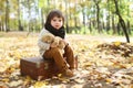 Cute fashionably dressed boy sitting on suitcase in the autumn p