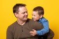 Cute father and son hugging on yellow background. Portrait of a dad with a baby boy smiling and hugging. Family concept Royalty Free Stock Photo