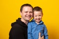 Cute father and son hugging on yellow background. Portrait of a dad with a baby boy smiling and hugging Royalty Free Stock Photo