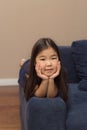 Cute female face portrait of little smiling girl, pretty adorable asian child lying on blue couch at home, look at cam Royalty Free Stock Photo