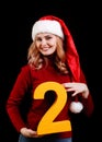 Cute female Santa in a red cap, holding number two on a black background. 2018 year holiday concept. Royalty Free Stock Photo