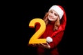 Cute female Santa in a red cap, holding number two on a black background. 2018 year holiday concept. Royalty Free Stock Photo