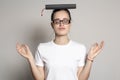 Cute female student woman with glasses meditating, she closed her eyes and put the book on his head like a cap graduate. Education Royalty Free Stock Photo